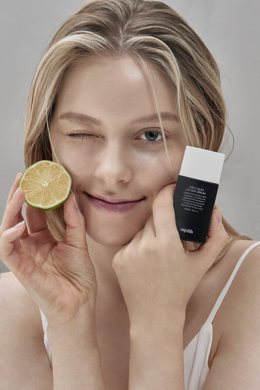 Smiling woman with blonde hair holding lime and black sun serum bottle in skincare beauty photo