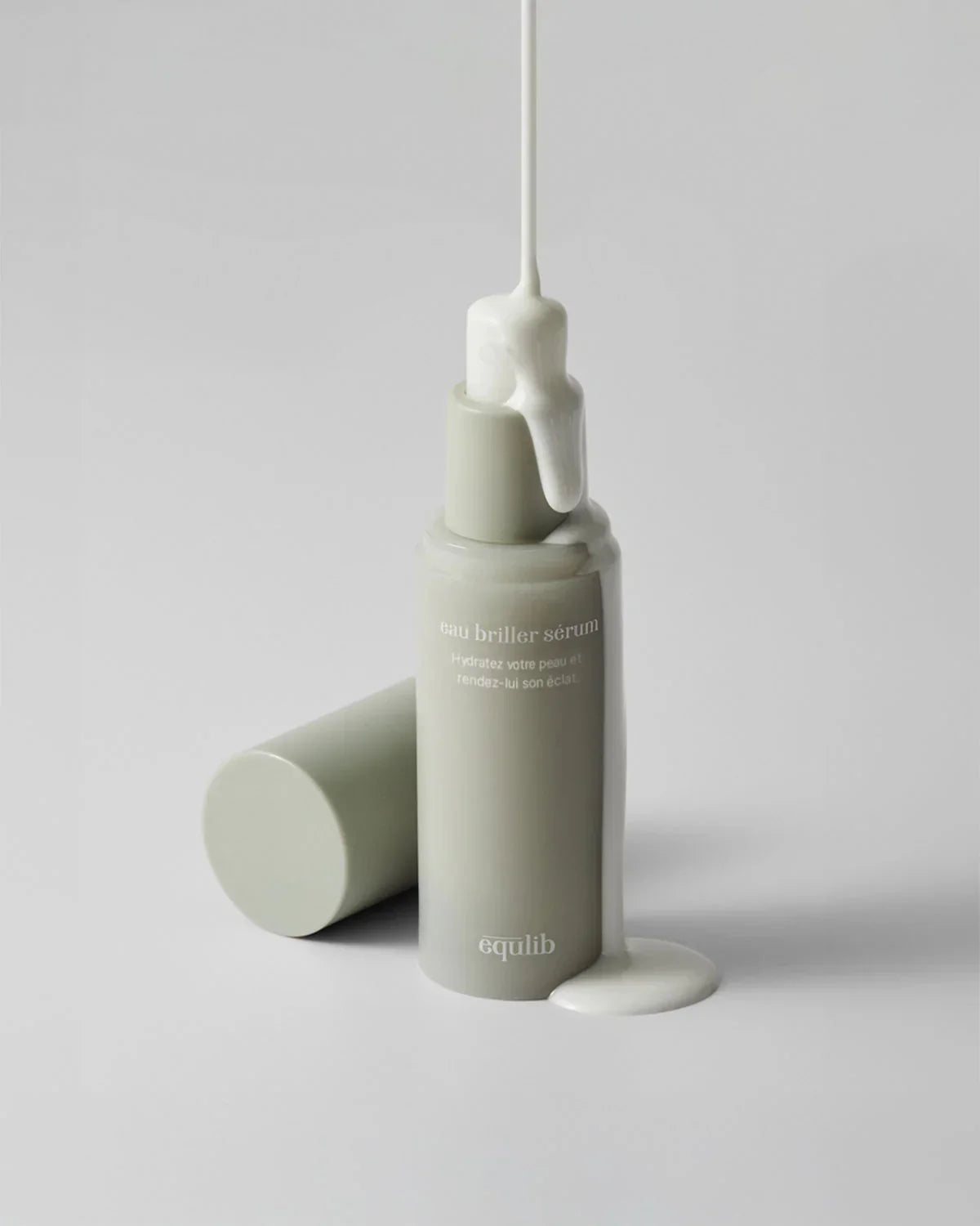 Minimalist gray bottle of Equilib eau briller sérum with creamy white serum dripping down